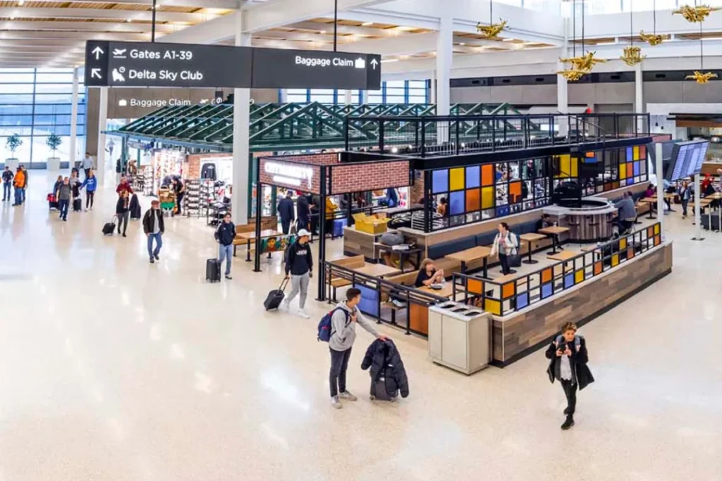 Interior view of JFK Terminal 1 with travelers, dining areas, and retail shops, services available for Austrian Airlines passengers.
