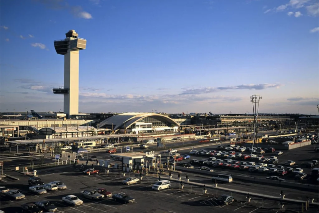 A wide view of JFK Airport Terminal 1 with control tower and nearby parking areas for Austrian Airlines passengers.
